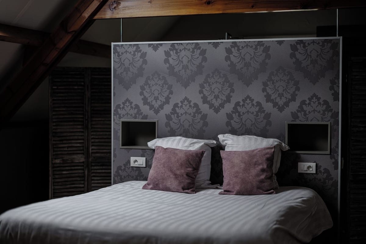 Quarto com uma cama, duas almofadas, uma televisão e uma tomada.