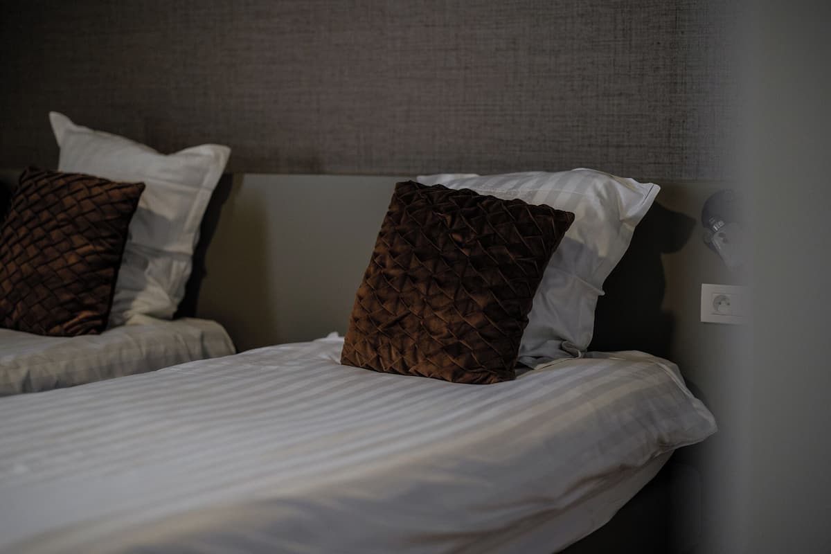 Cama com roupa de cama branca e duas almofadas decorativas.