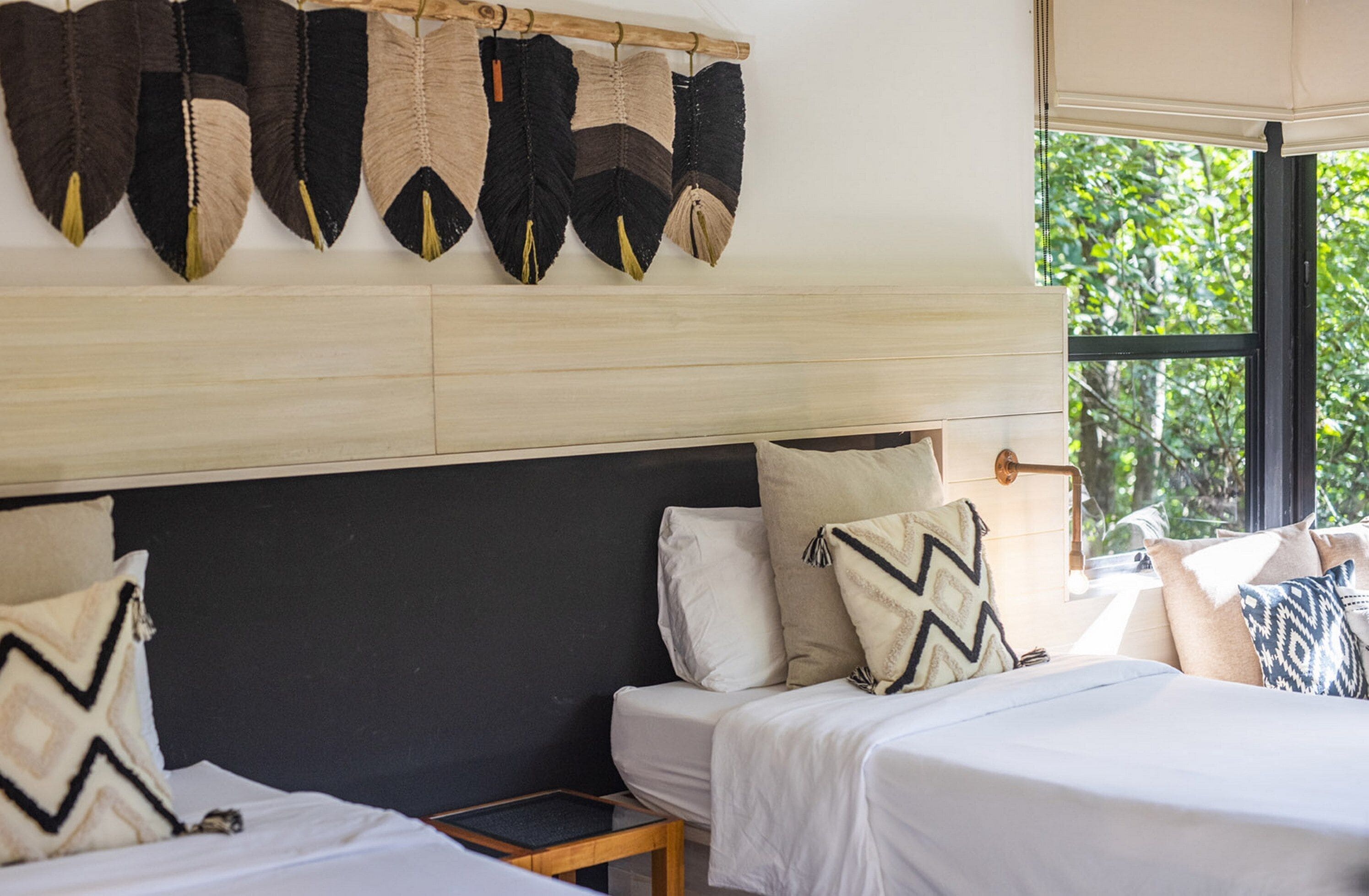 A bedroom with two beds, a wooden headboard, and a window with a view of greenery.