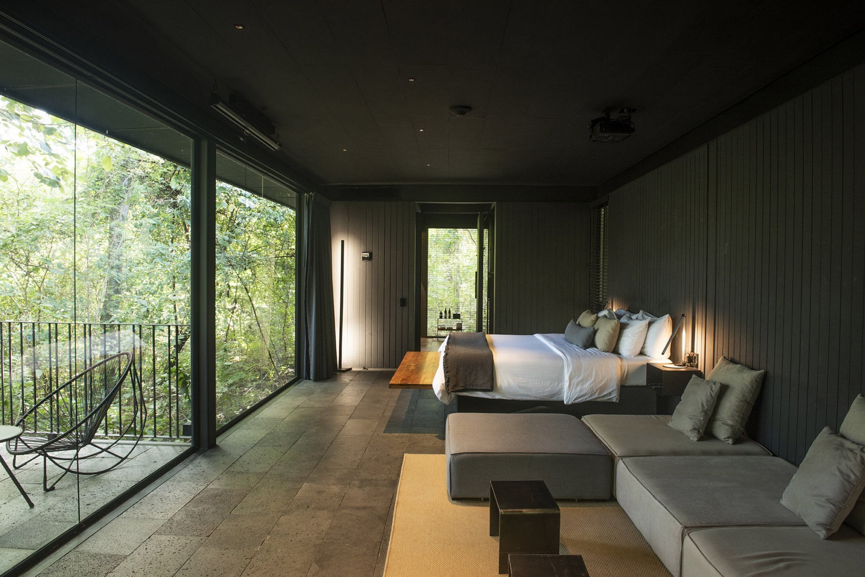 A modern bedroom with a large bed, a sofa, and a balcony with a chair.