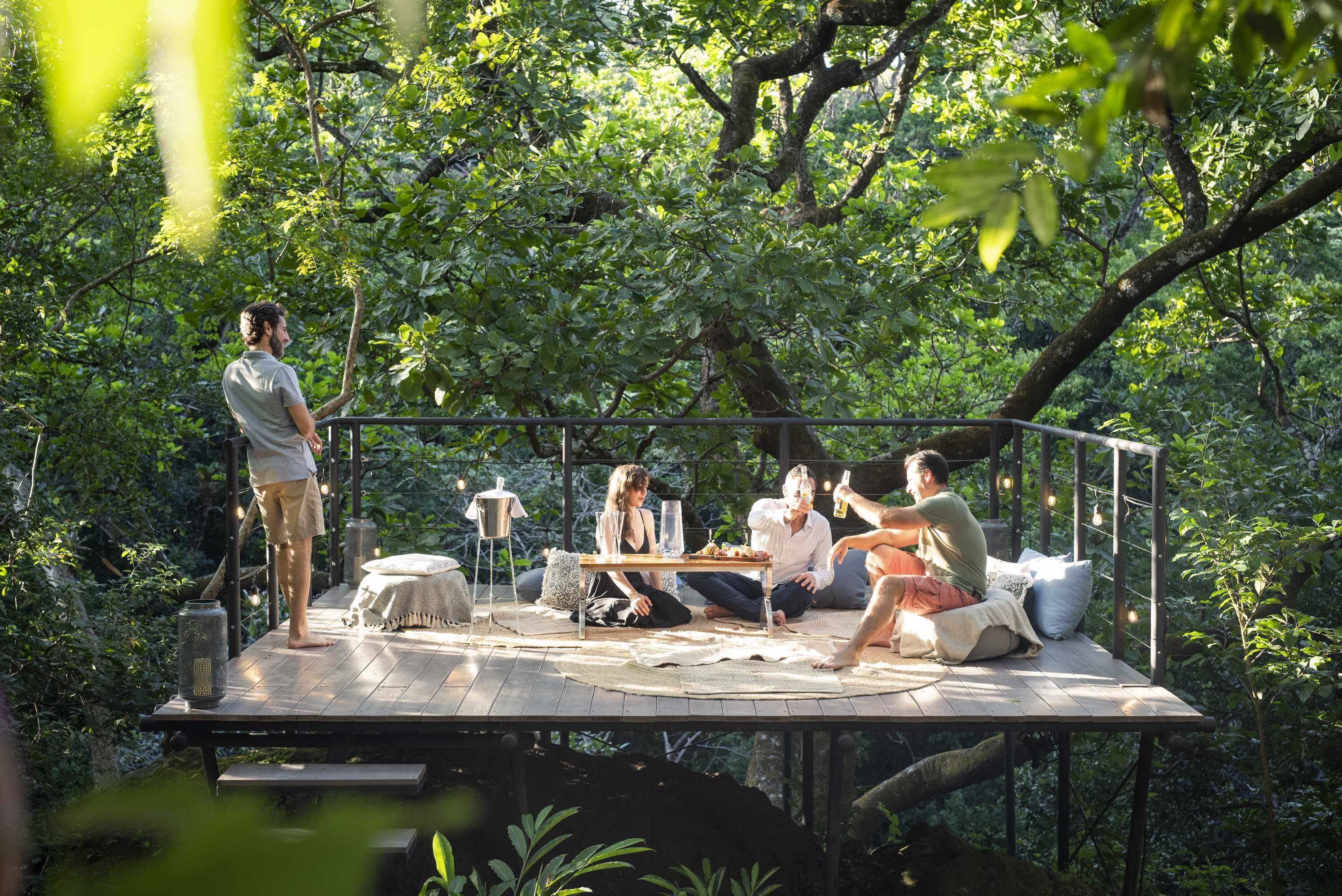 A wooden deck with a table and chairs, surrounded by lush greenery.