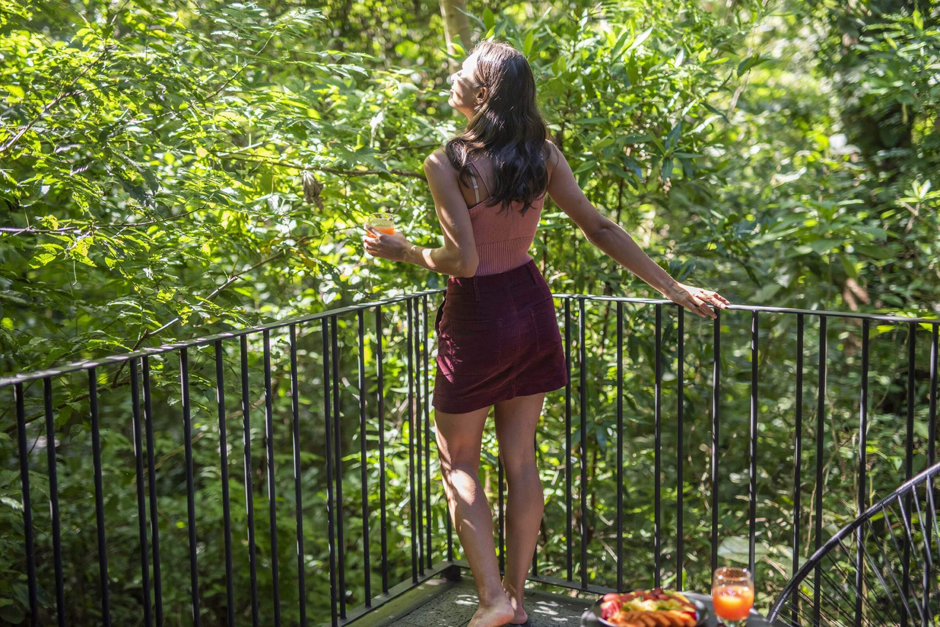 A person standing on a balcony with a railing, surrounded by lush greenery.