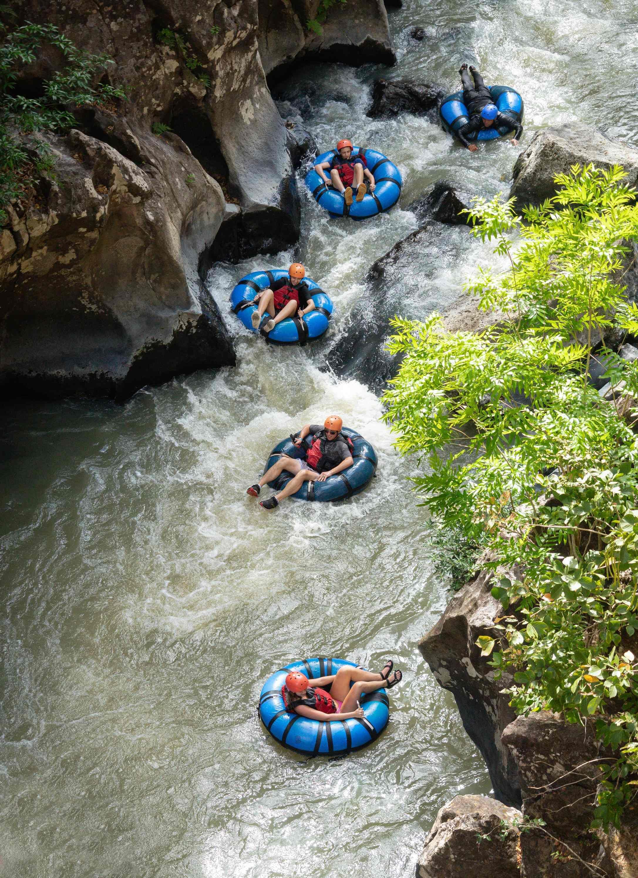 People rafting down a river surrounded by rocky cliffs and greenery.