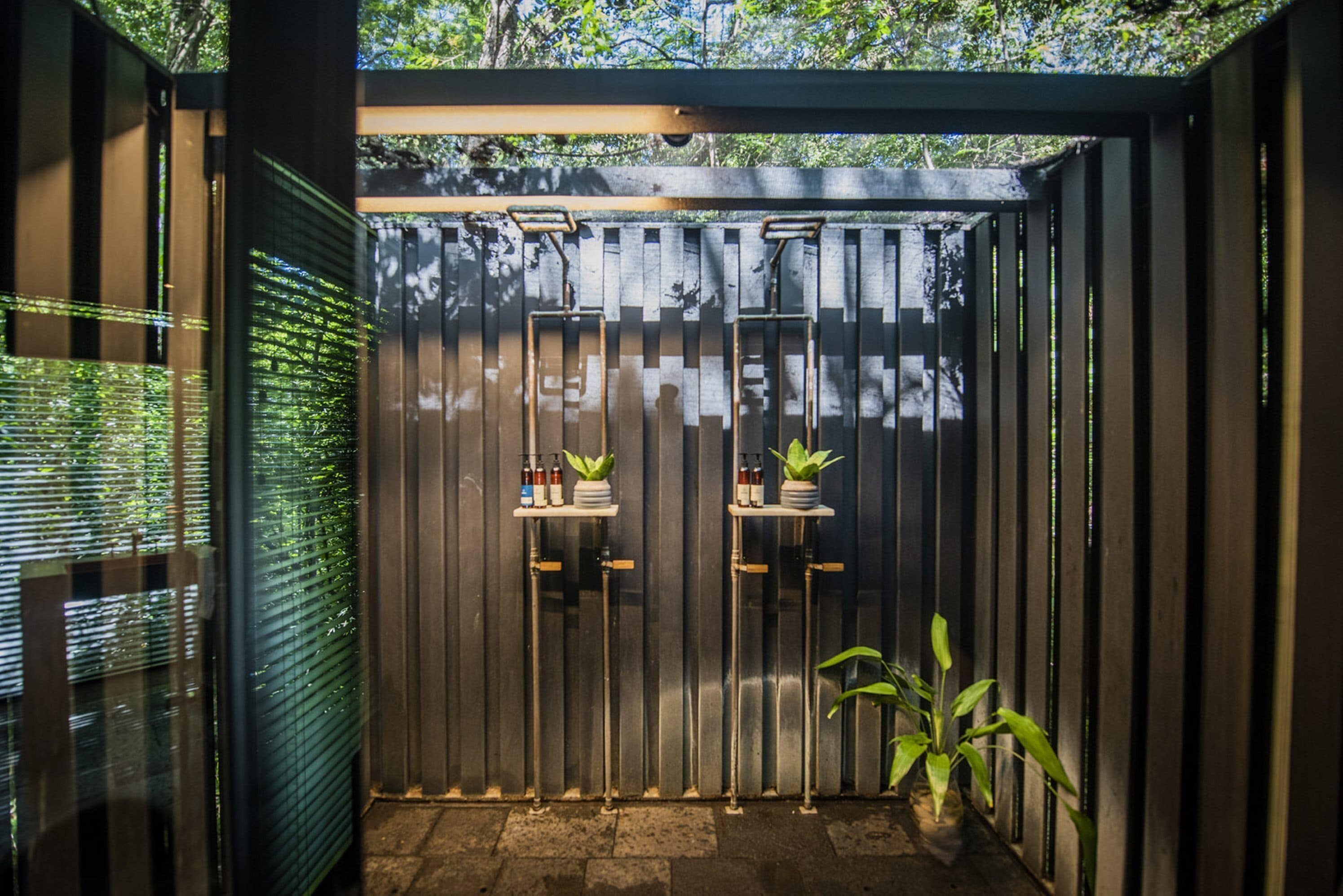 A covered outdoor area with a metal gate, two small tables with potted plants, and a potted plant to the right.