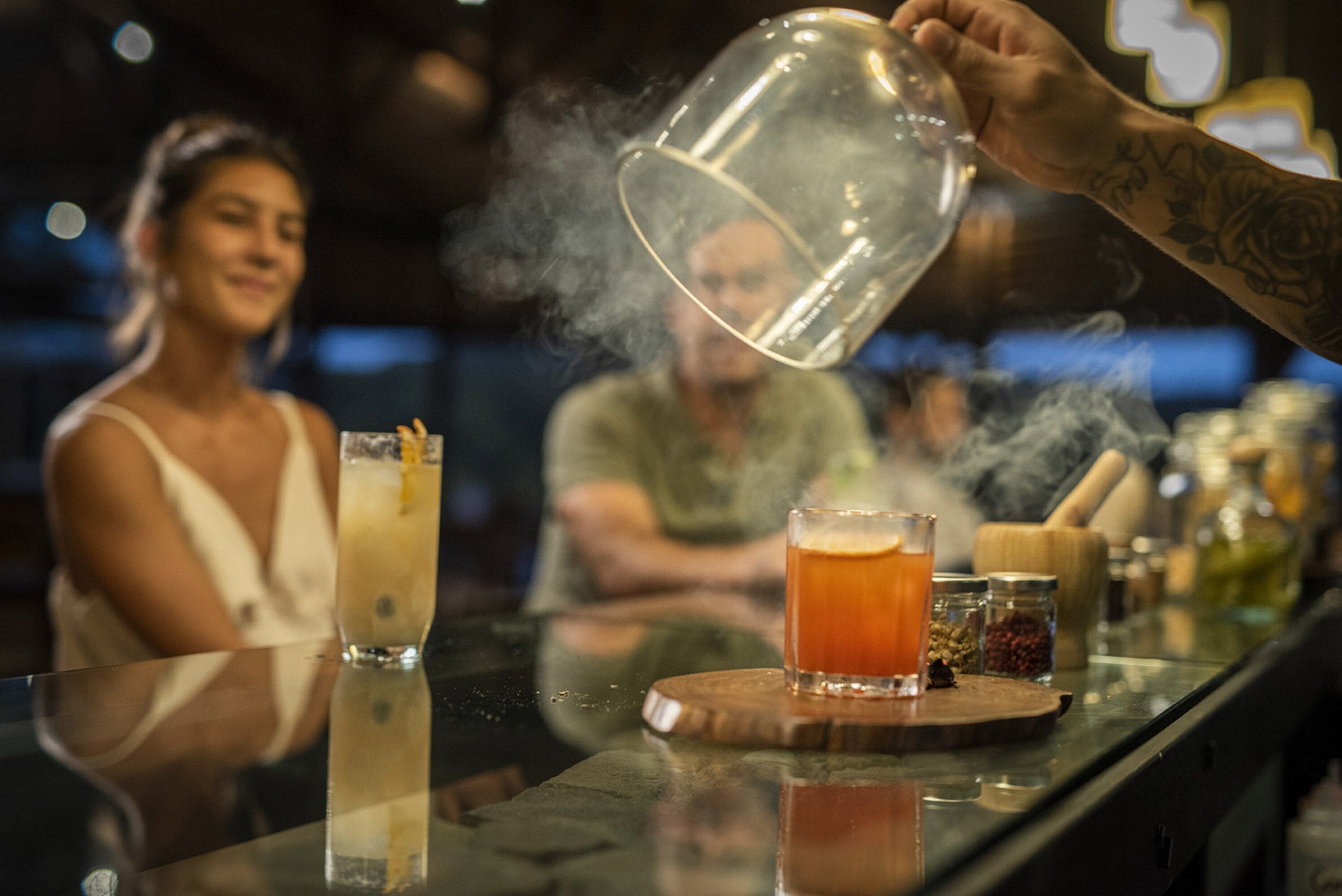Un bar con una persona sirviendo una bebida en un vaso, una barra y diferentes botellas y frascos sobre la barra.