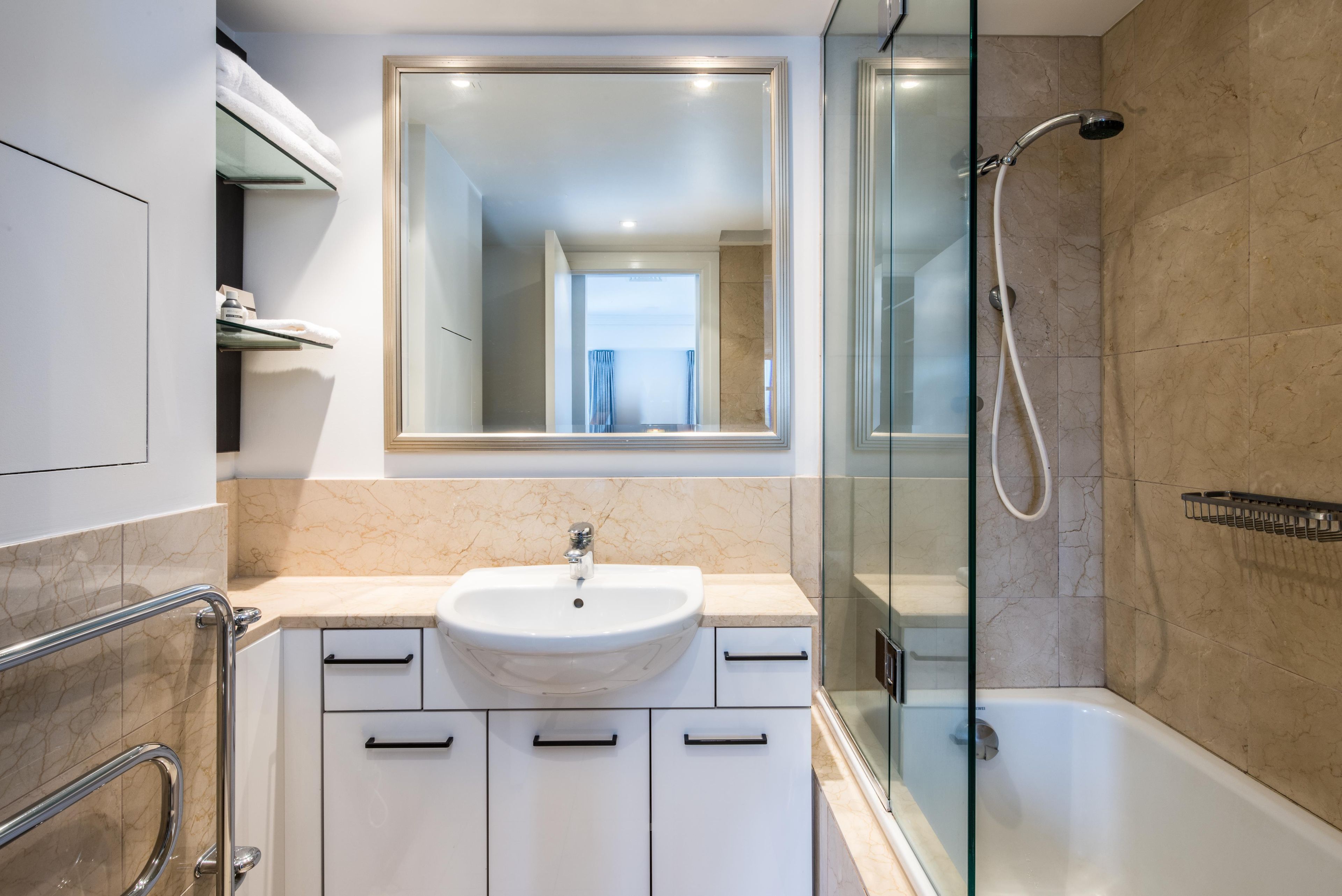 A modern bathroom with a glass shower enclosure, a white sink, and a large mirror.