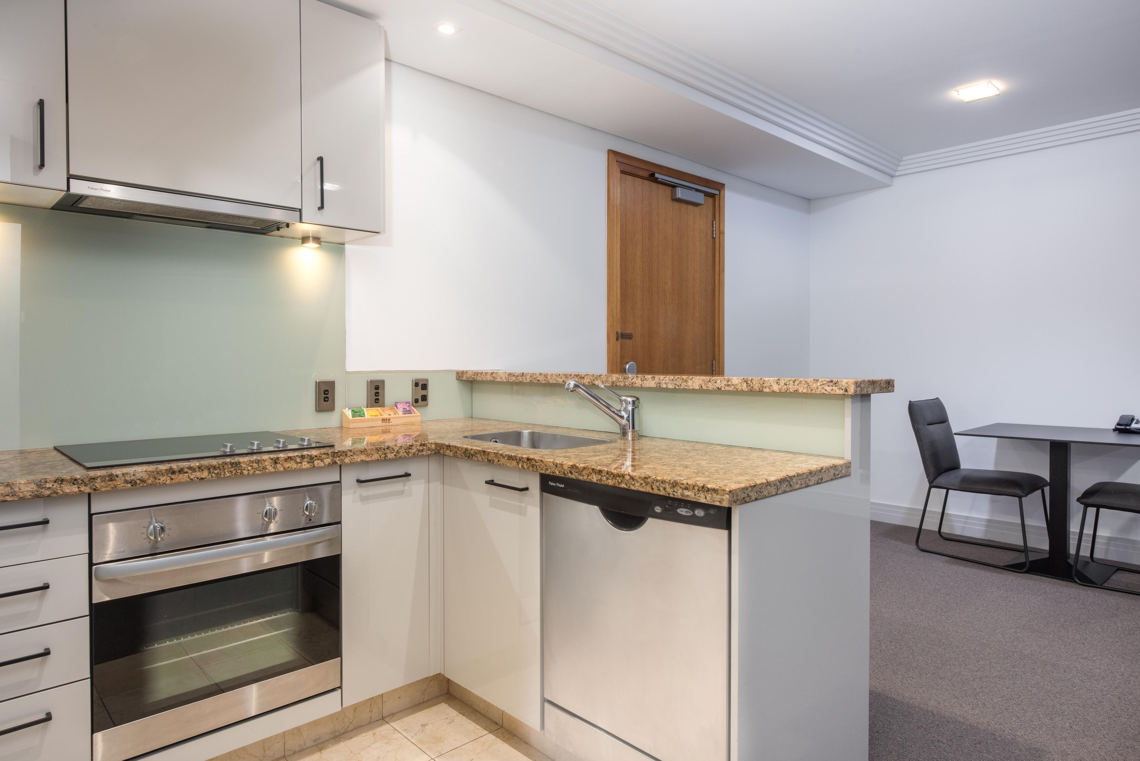 A compact kitchen with a built-in oven, a dishwasher, and a granite countertop.