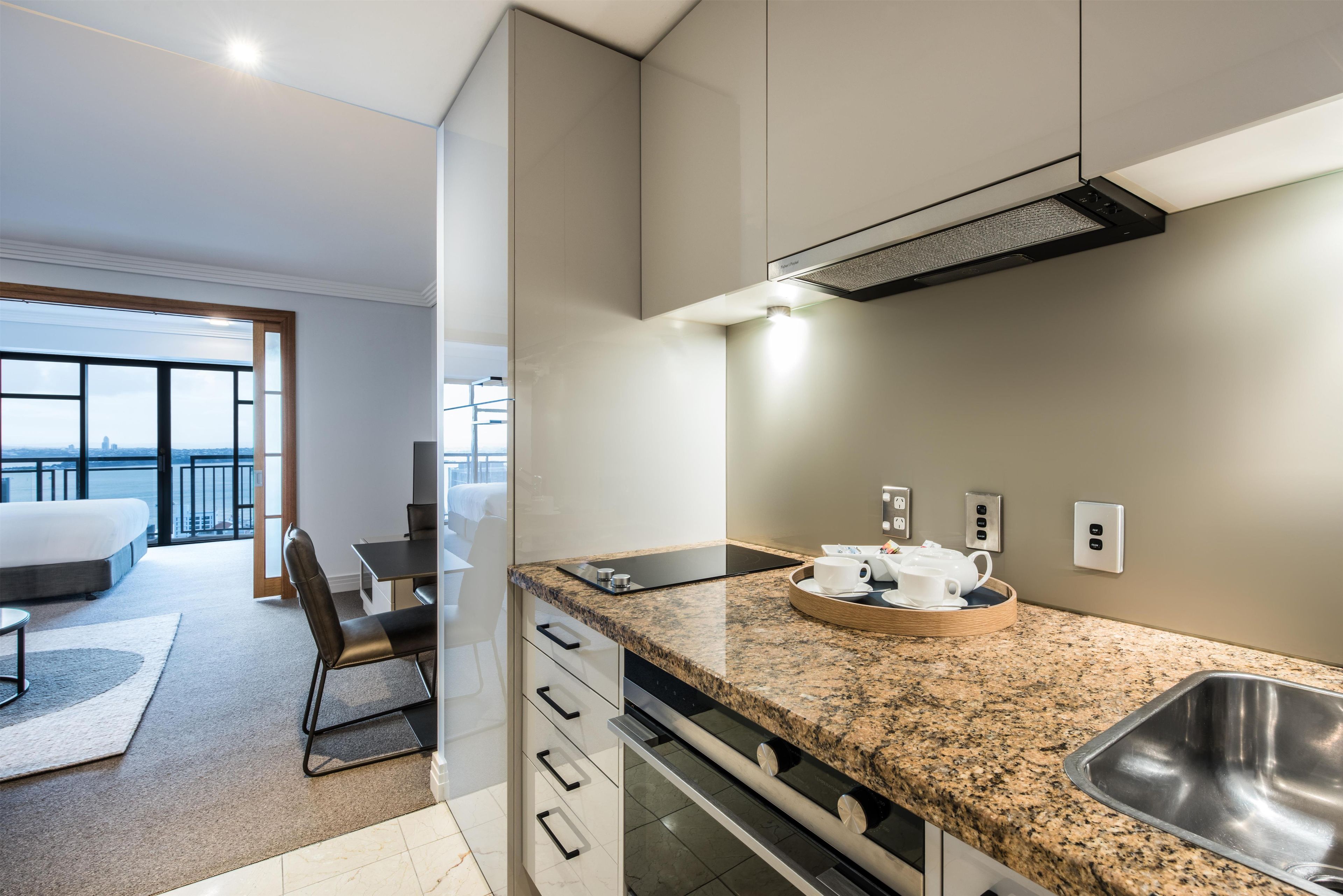 A modern kitchen with a granite countertop, stainless steel sink, and a view of the city through large windows.