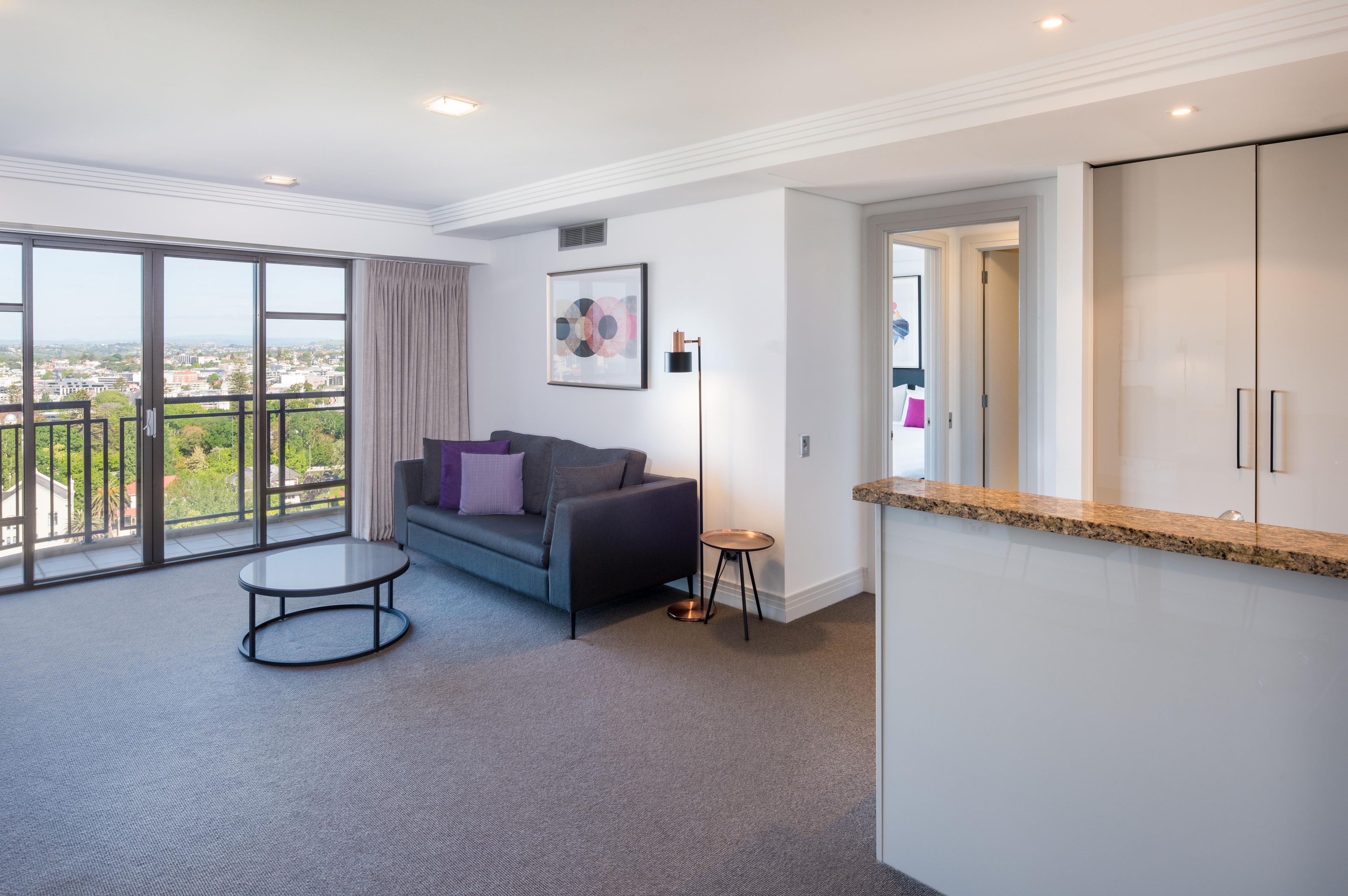 Ein modernes Wohnzimmer mit einer Couch, einem kleinen runden Tisch und einem großen Fenster mit Blick auf die Stadt.