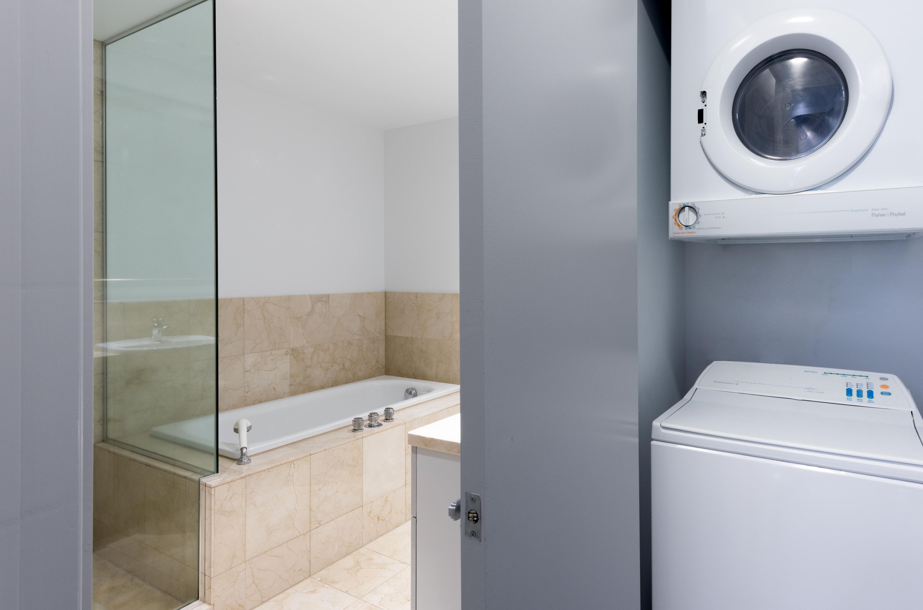 A modern bathroom with a glass shower enclosure, a bathtub, and a front-loading washing machine.