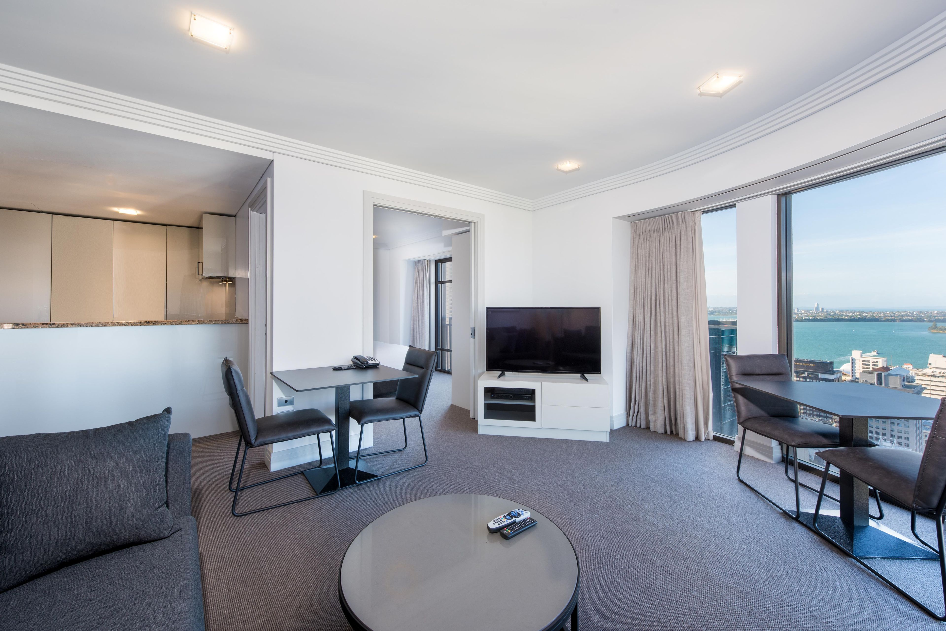 Habitación de hotel moderna con balcón, zona de comedor, televisión y vistas a la ciudad.
