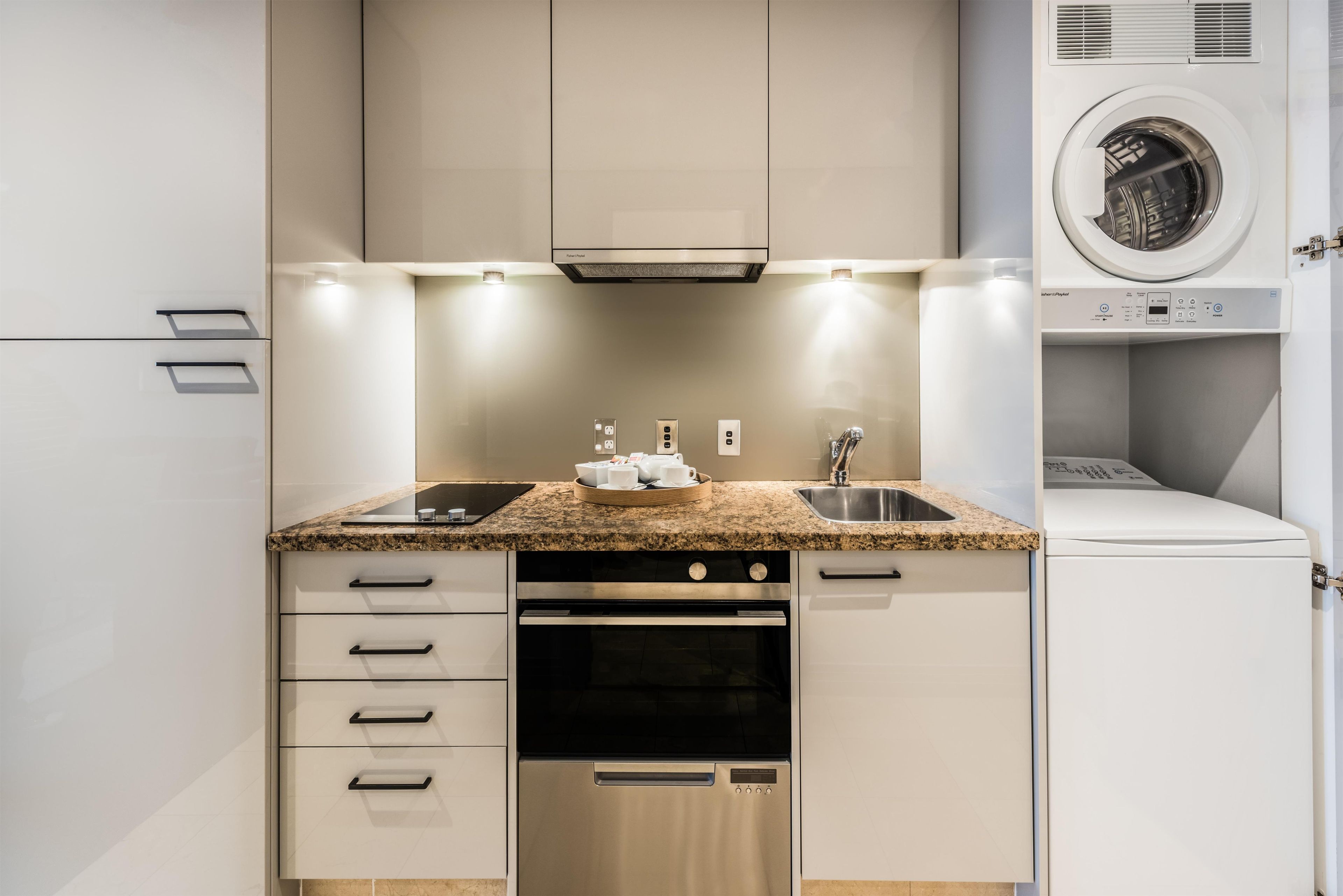 A modern kitchen with a granite countertop, stainless steel appliances, and a built-in washer and dryer.