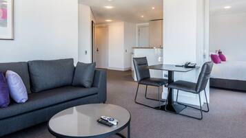 Una habitación de hotel moderna con un sofá gris, una mesa redonda y un comedor con una mesa y sillas.