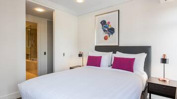 A hotel room with a large bed, a nightstand, a wall-mounted artwork, and a door leading to a bathroom.