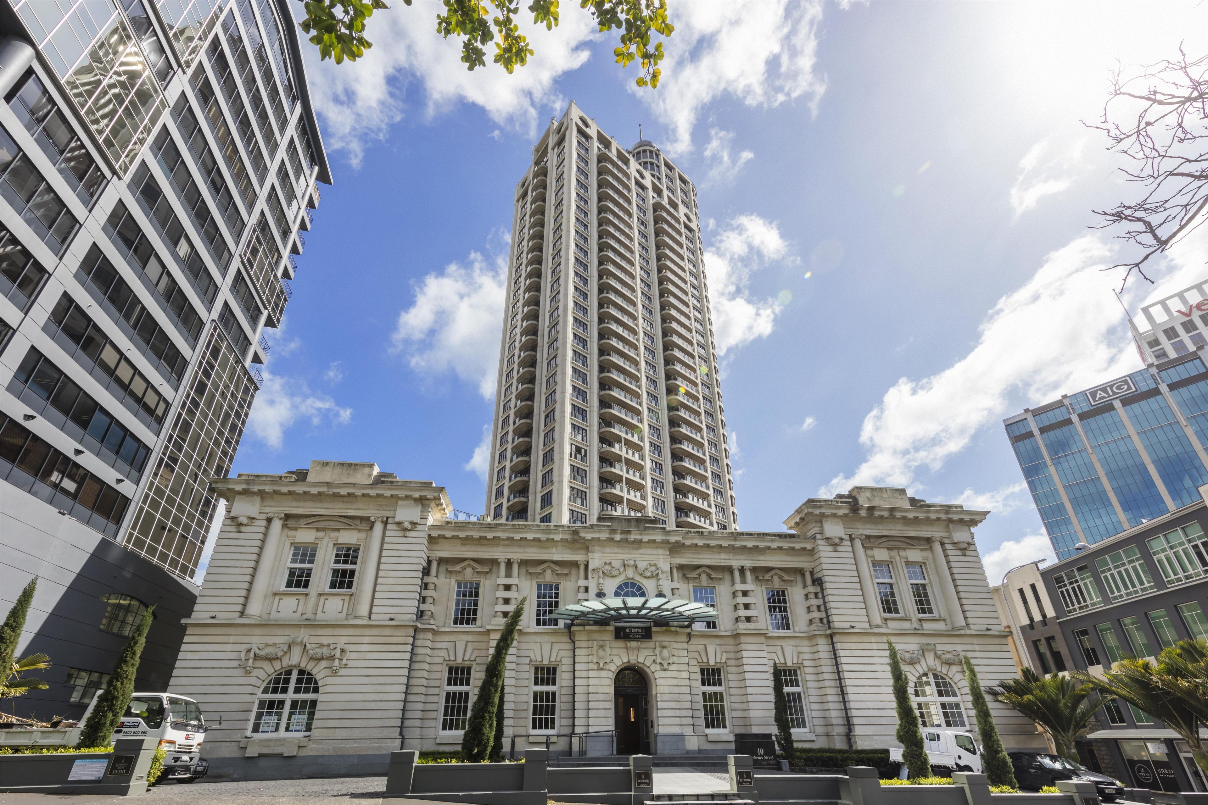 A historic building with a central entrance, flanked by modern high-rise buildings.