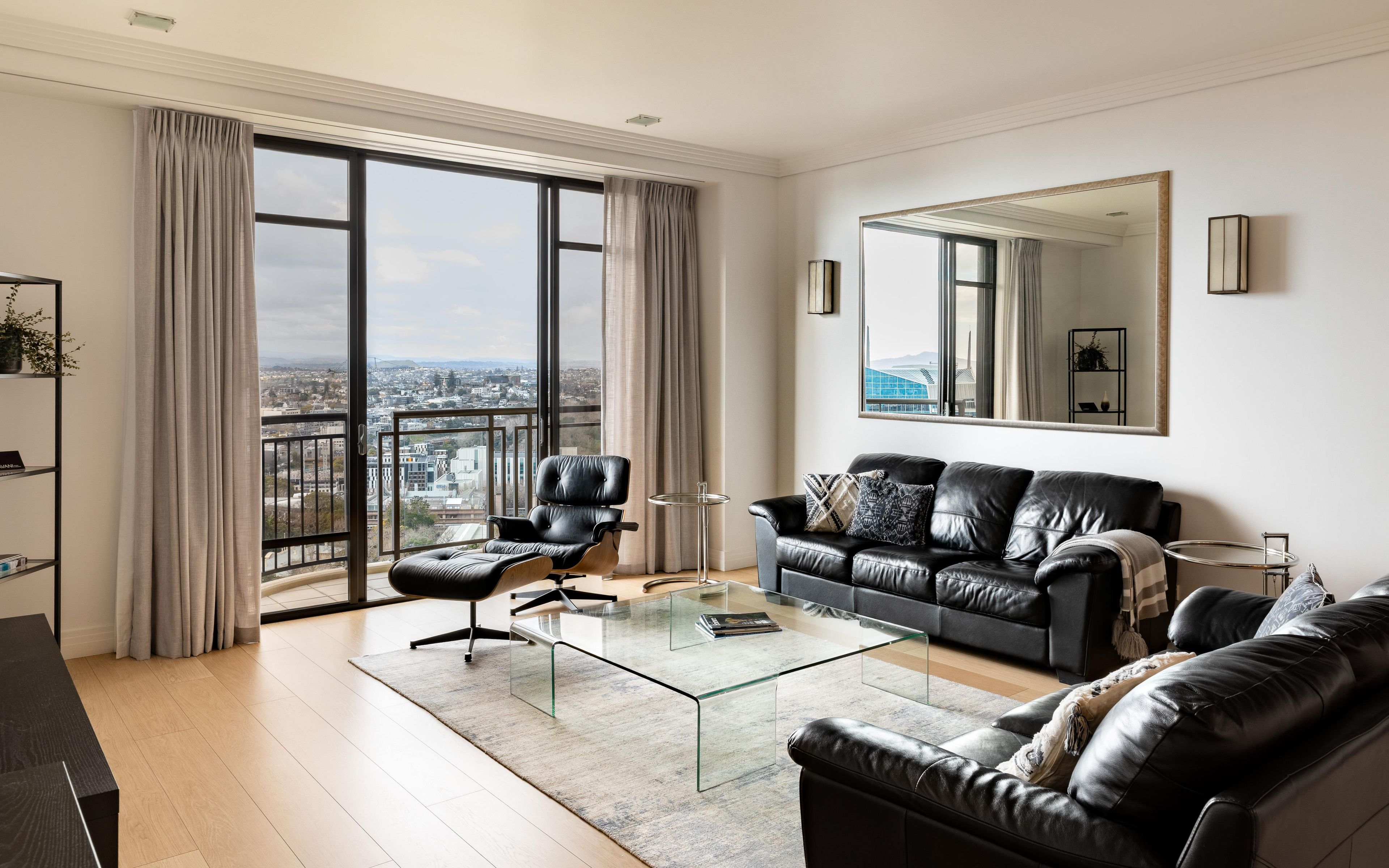 Una sala de estar moderna con un sofá de cuero, una mesa de centro de vidrio y un ventanal con vista a la ciudad.