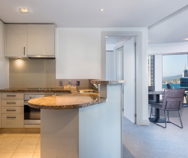 A modern kitchen with granite countertops, stainless steel appliances, and a view of a cityscape through large windows. - Avani Auckland Metropolis Residences (Auckland)