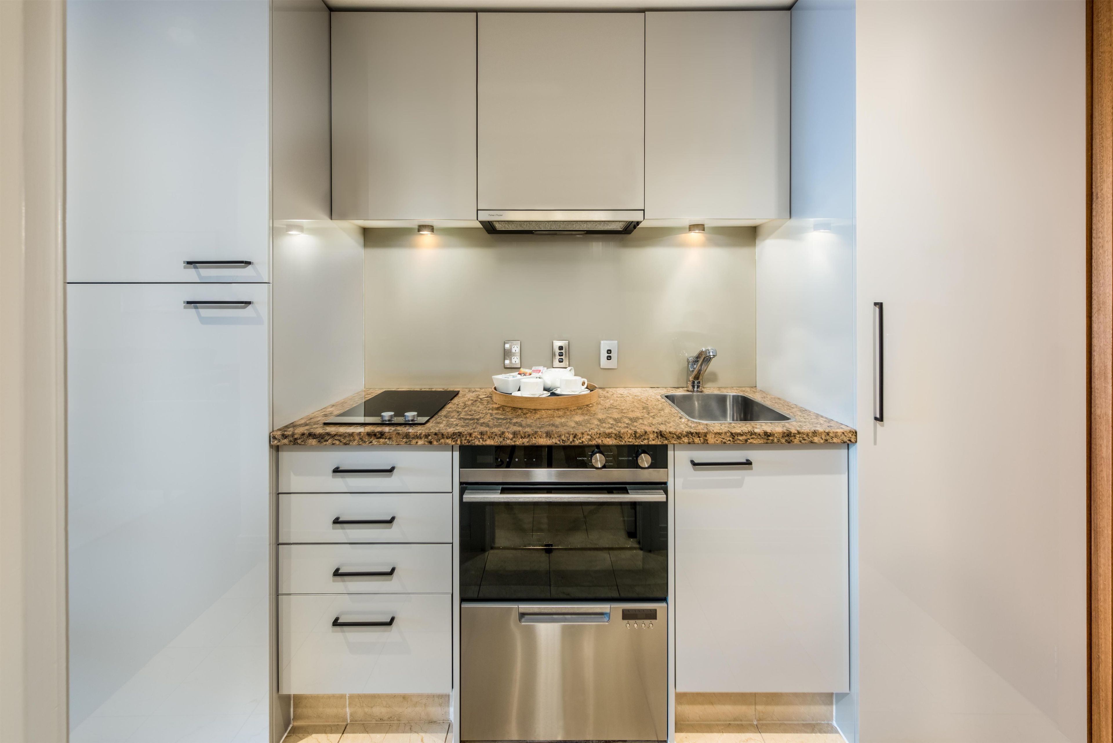 A compact kitchen with white cabinets, a granite countertop, stainless steel appliances, and a built-in oven.