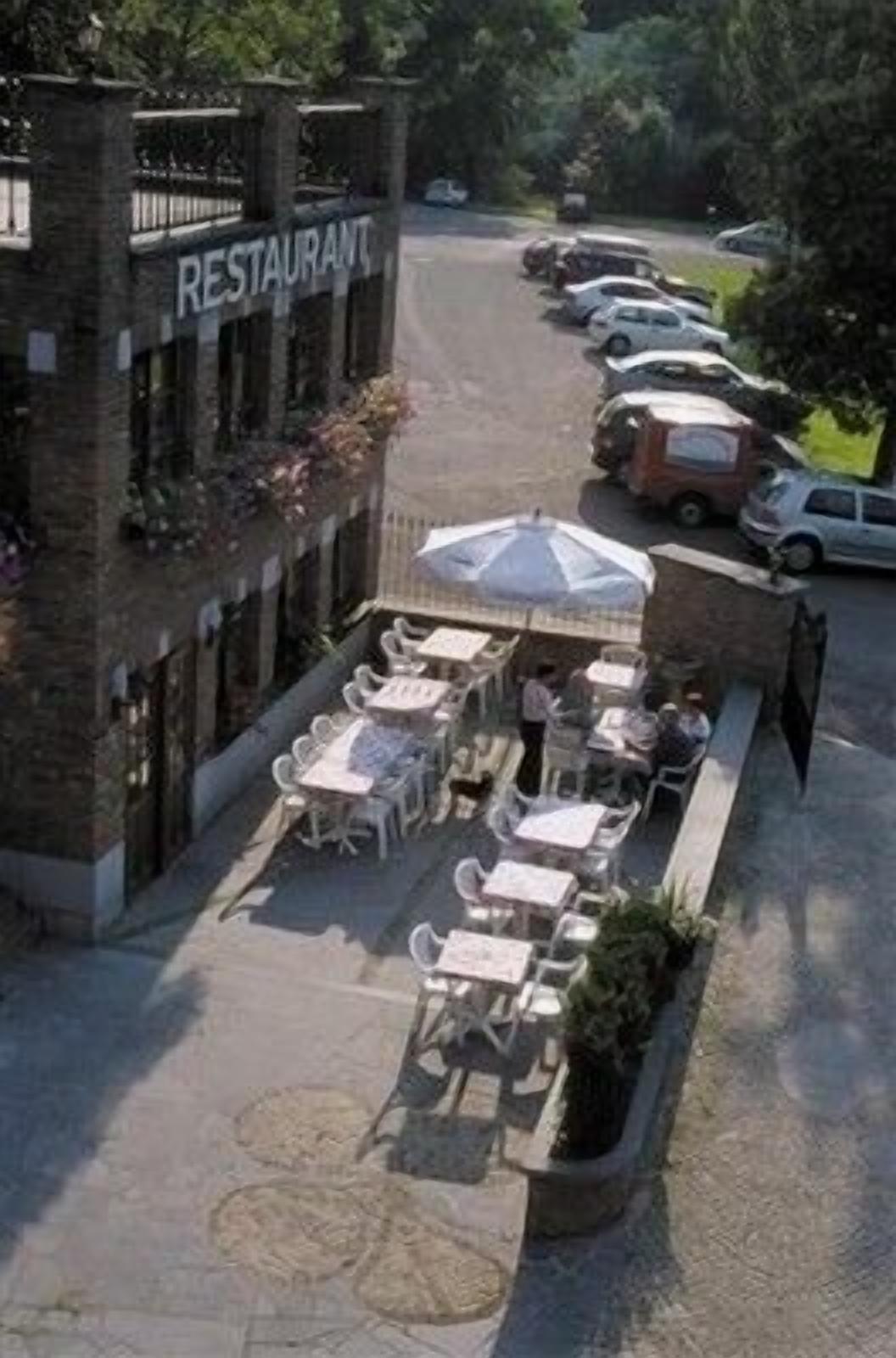 Un restaurante con terraza, fachada de ladrillo y coches estacionados al fondo.