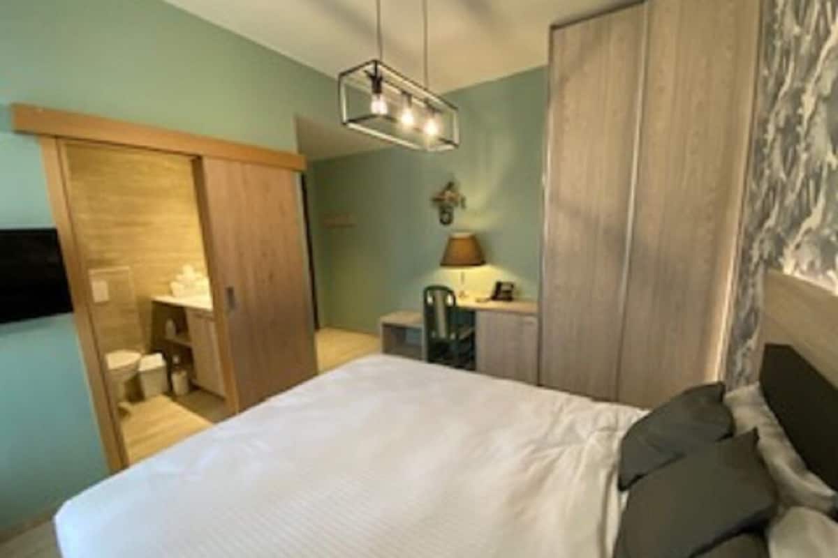 A bedroom with a bed, a wardrobe, a desk, and a lamp.