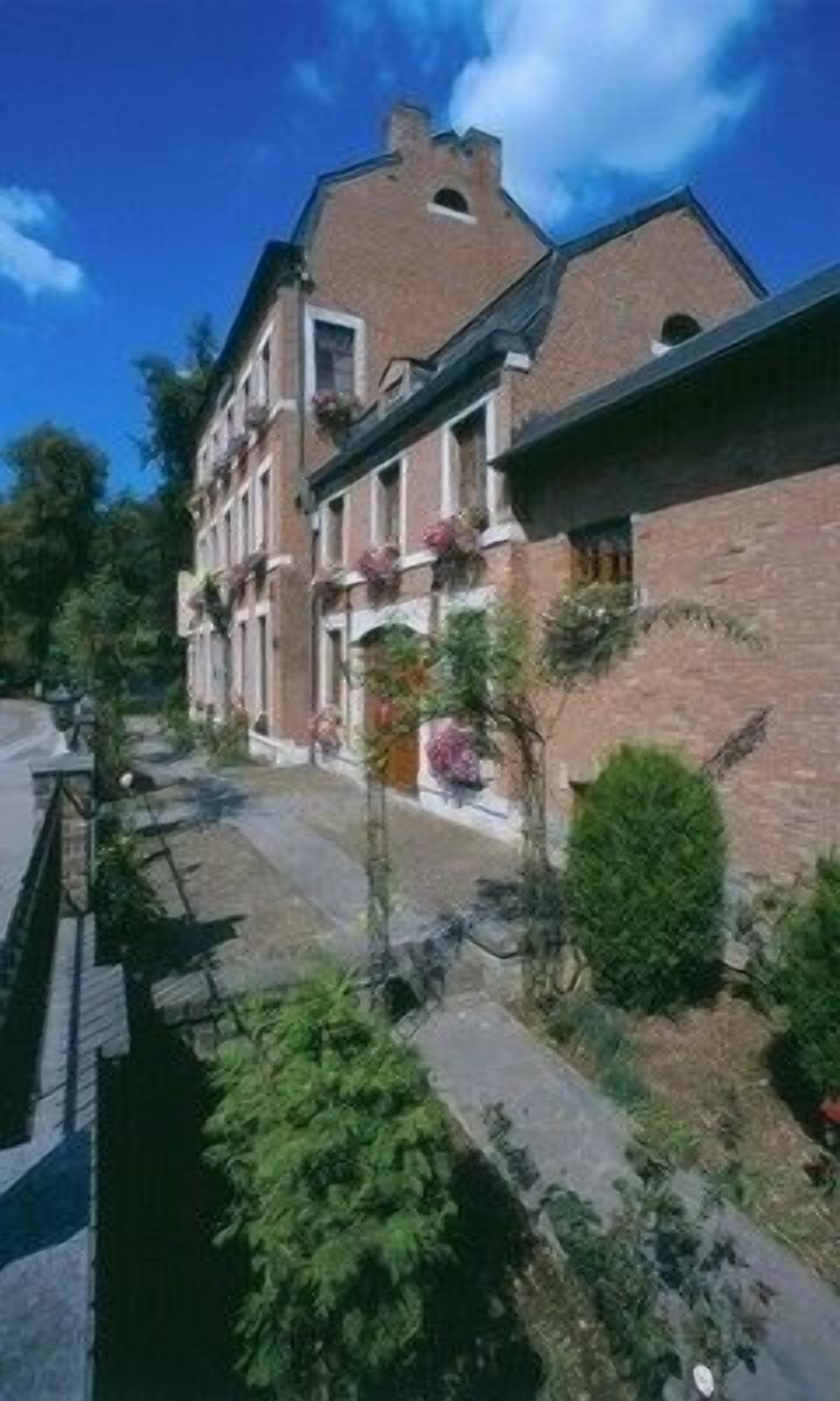 A two-story brick building with a sloped roof, multiple windows, and a small garden area with various plants and flowers.