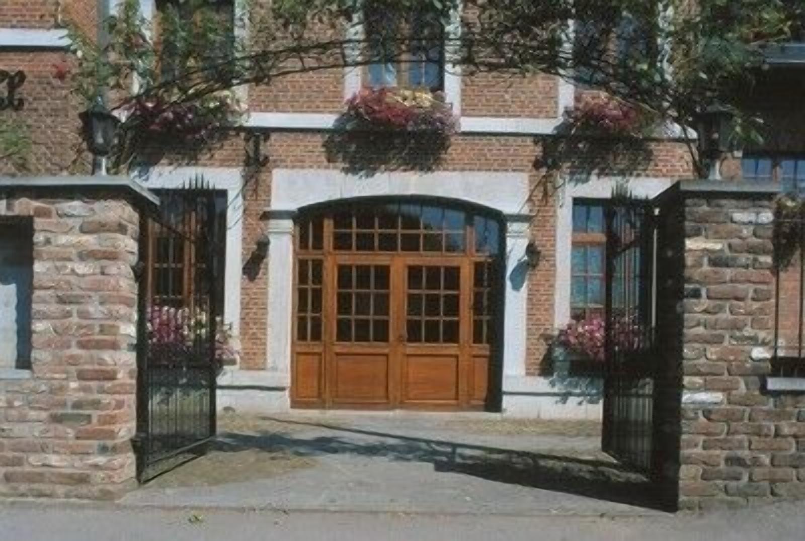 Un bâtiment en briques doté d’une grande porte en bois, de deux fenêtres et d’un petit porche.