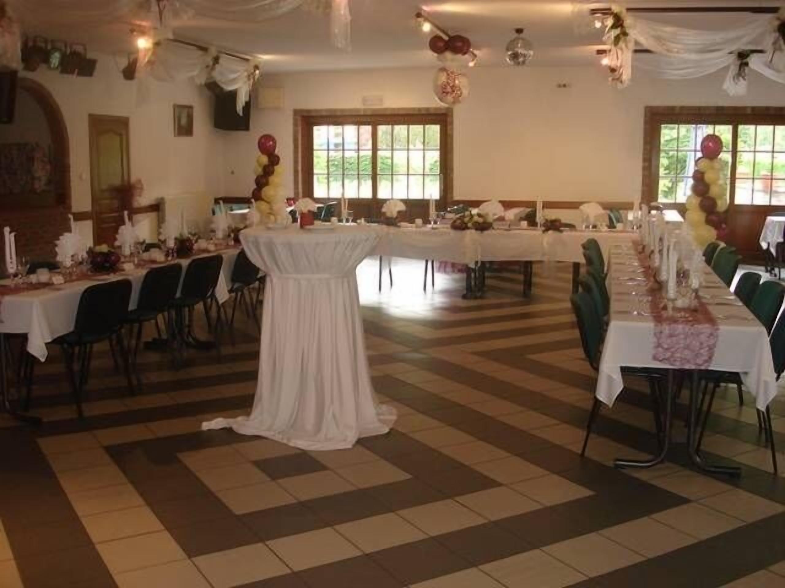 A banquet hall with multiple tables set for a formal event, featuring a tiled floor and large windows.