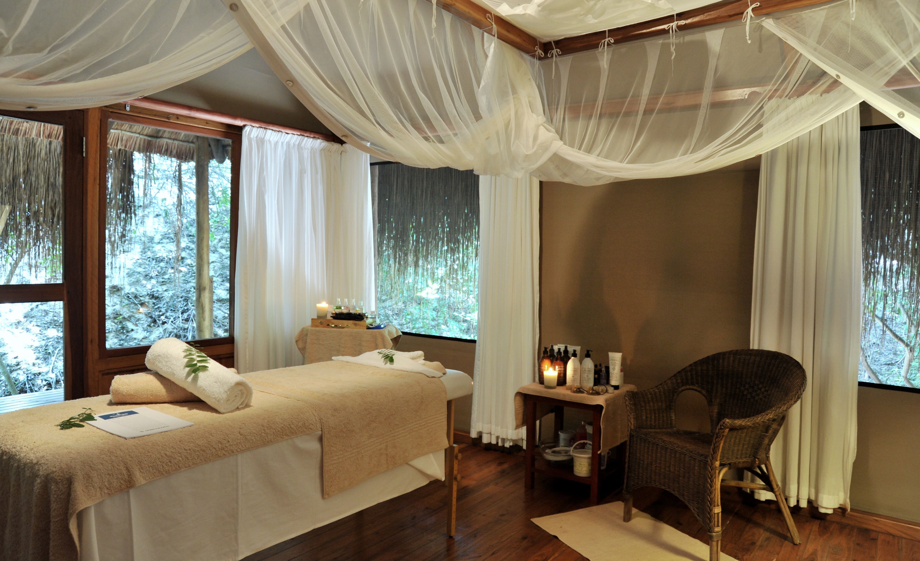 Una habitación con cama, una silla, una mesa con artículos de aseo y ventanas con cortinas.
