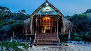 A thatched-roof building labeled "Machangulo Beach Lodge" with a staircase leading to the entrance.