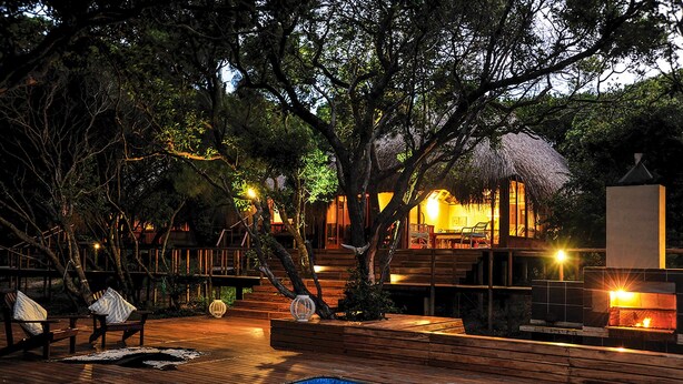 A wooden deck with a pool, outdoor seating, and a thatched-roof structure.