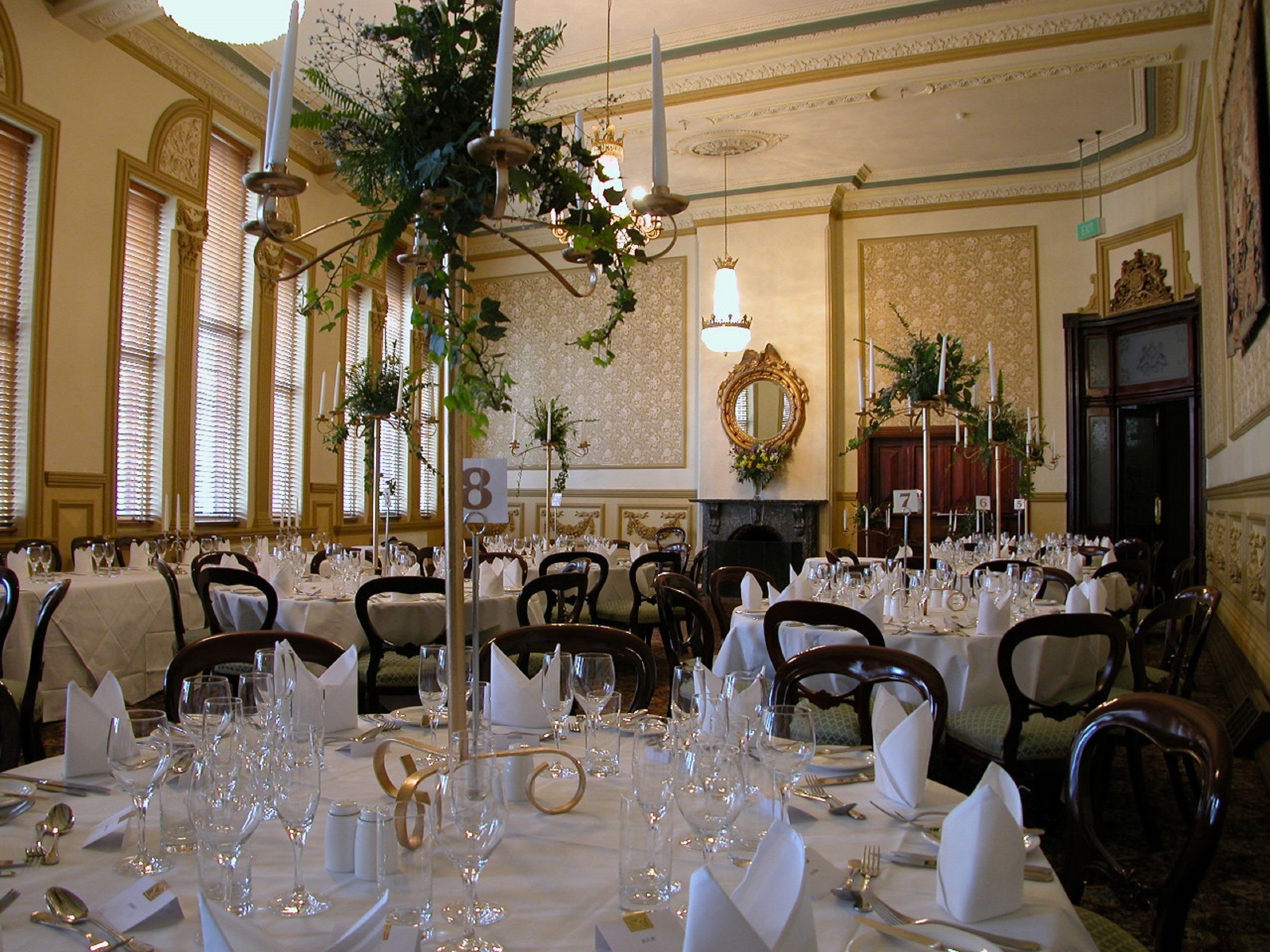 A banquet hall with multiple round tables set for dining, each with white tablecloths, glassware, and chairs.