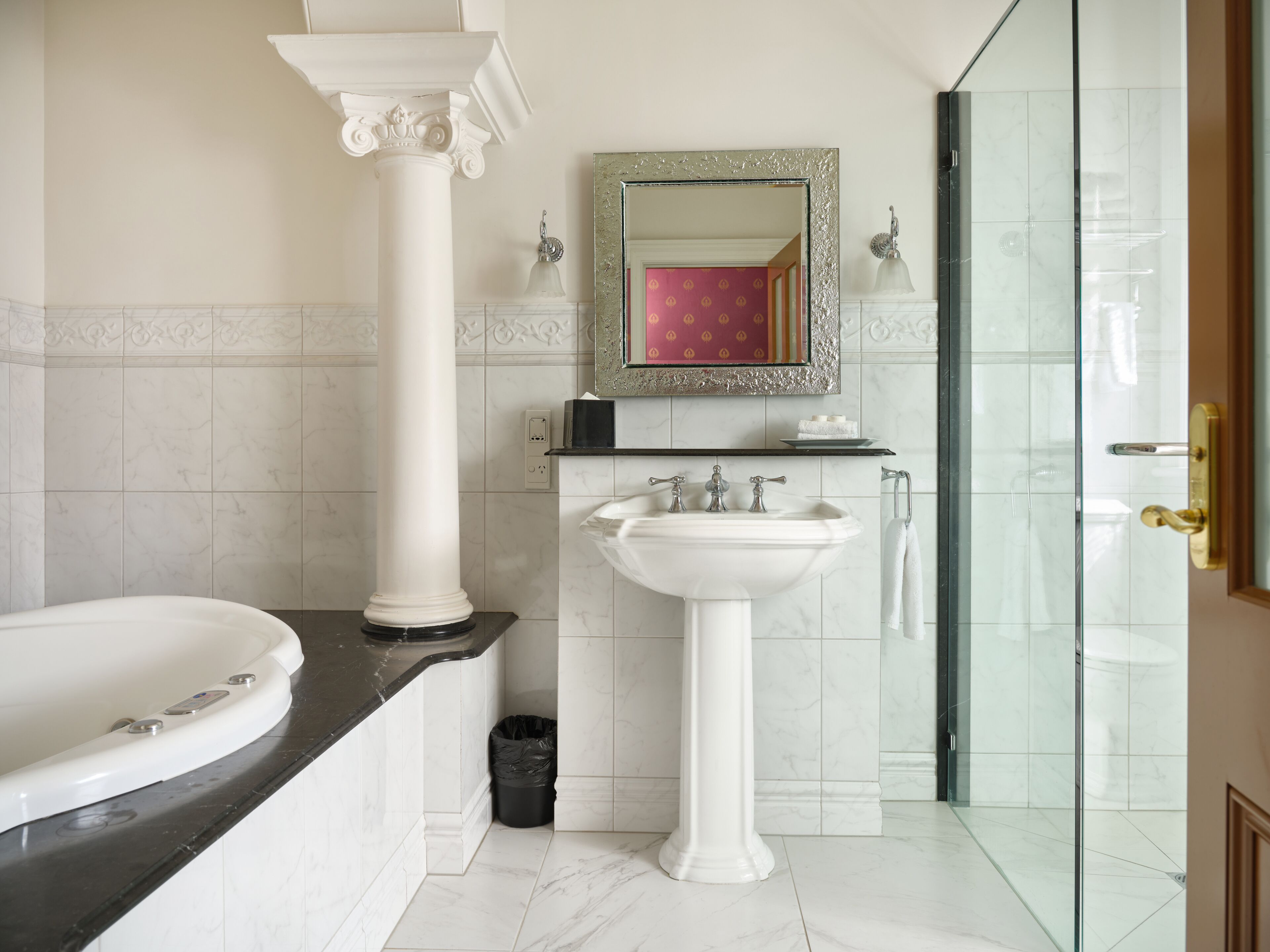 Un baño con bañera, lavamanos pedestal, espejo y zona de ducha.