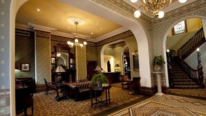 A grand lobby with ornate chandeliers, a patterned carpet, and a staircase.
