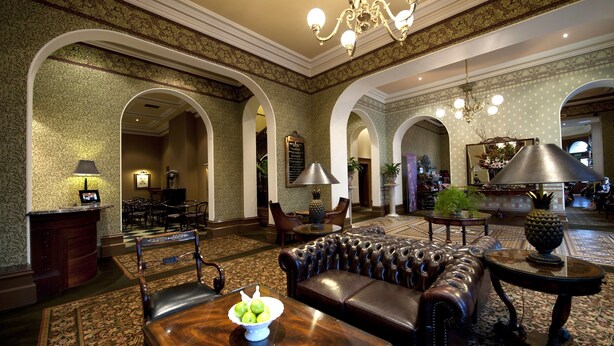 A lobby with a leather sofa, a wooden table with fruit, and a chandelier.