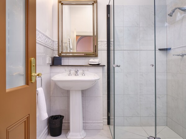 A bathroom with a white pedestal sink, a glass shower enclosure, and a gold-framed mirror. - Craig's Royal Hotel (Ballarat)