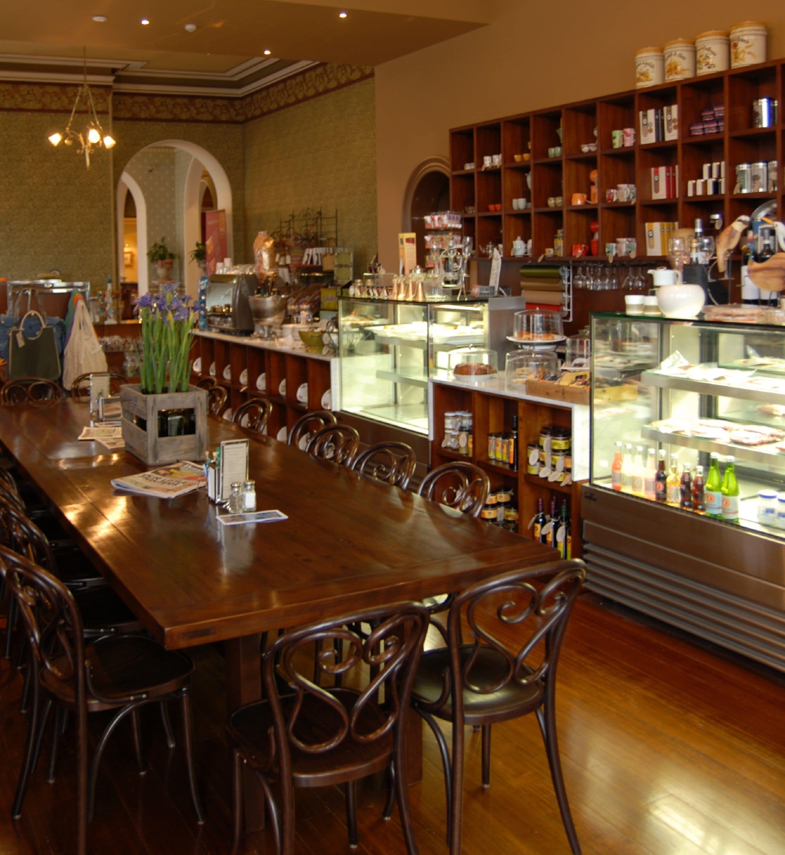 A restaurant with a long wooden table, chairs, and a display case with food items.