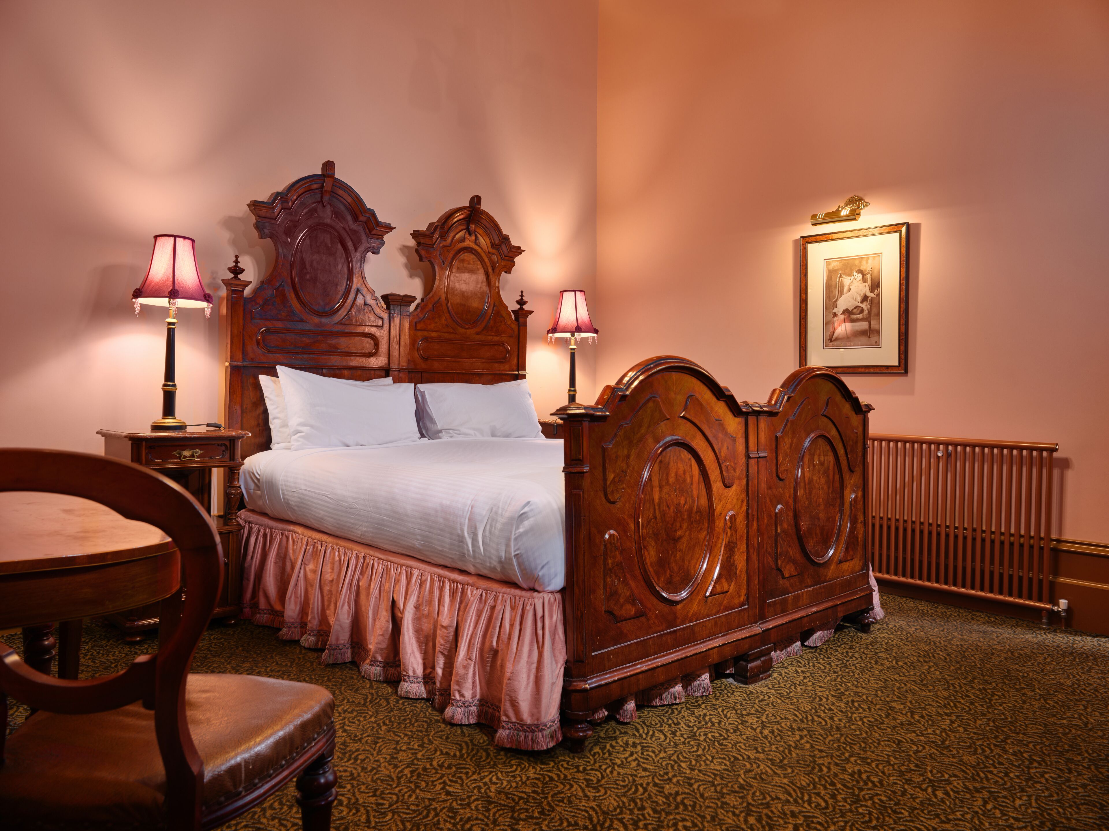 Une chambre à coucher de style traditionnel, avec un lit à baldaquin en bois, deux tables de chevet avec des lampes, une chaise et un radiateur.
