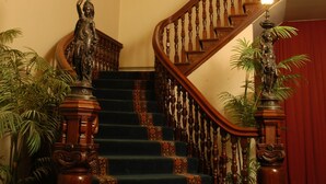 A grand staircase with ornate wooden balusters, a stained glass window above, and a red curtain at the bottom.