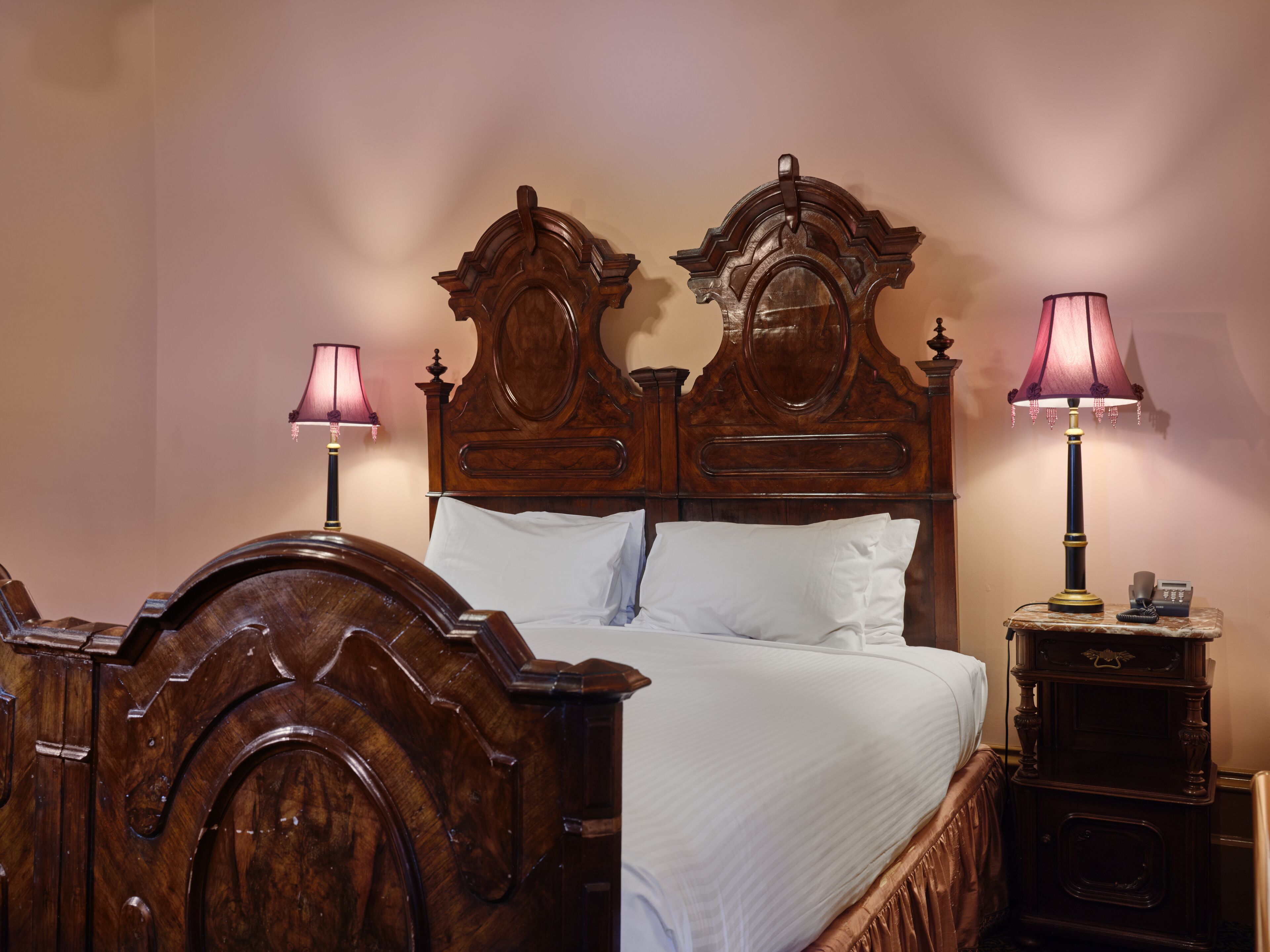 Ein hölzernes Himmelbett mit weißen Leinen, zwei Nachttischlampen und ein Nachttisch mit Telefon.