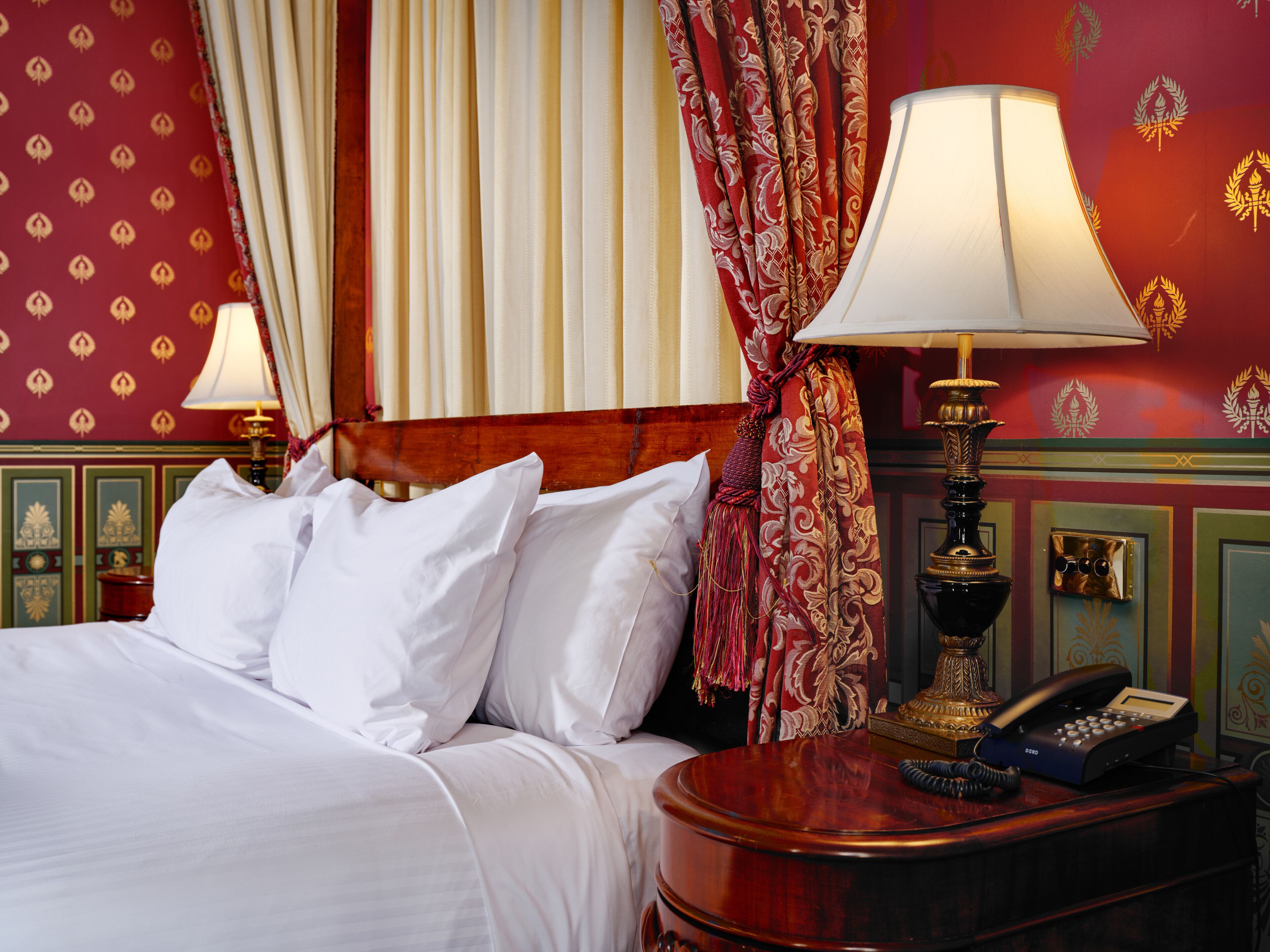 A hotel room with a neatly made bed, a bedside lamp, a telephone, and a decorative wall with a patterned design.