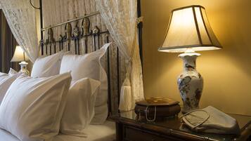 A neatly made bed with white linens, a lace canopy, and a bedside lamp with a floral vase.
