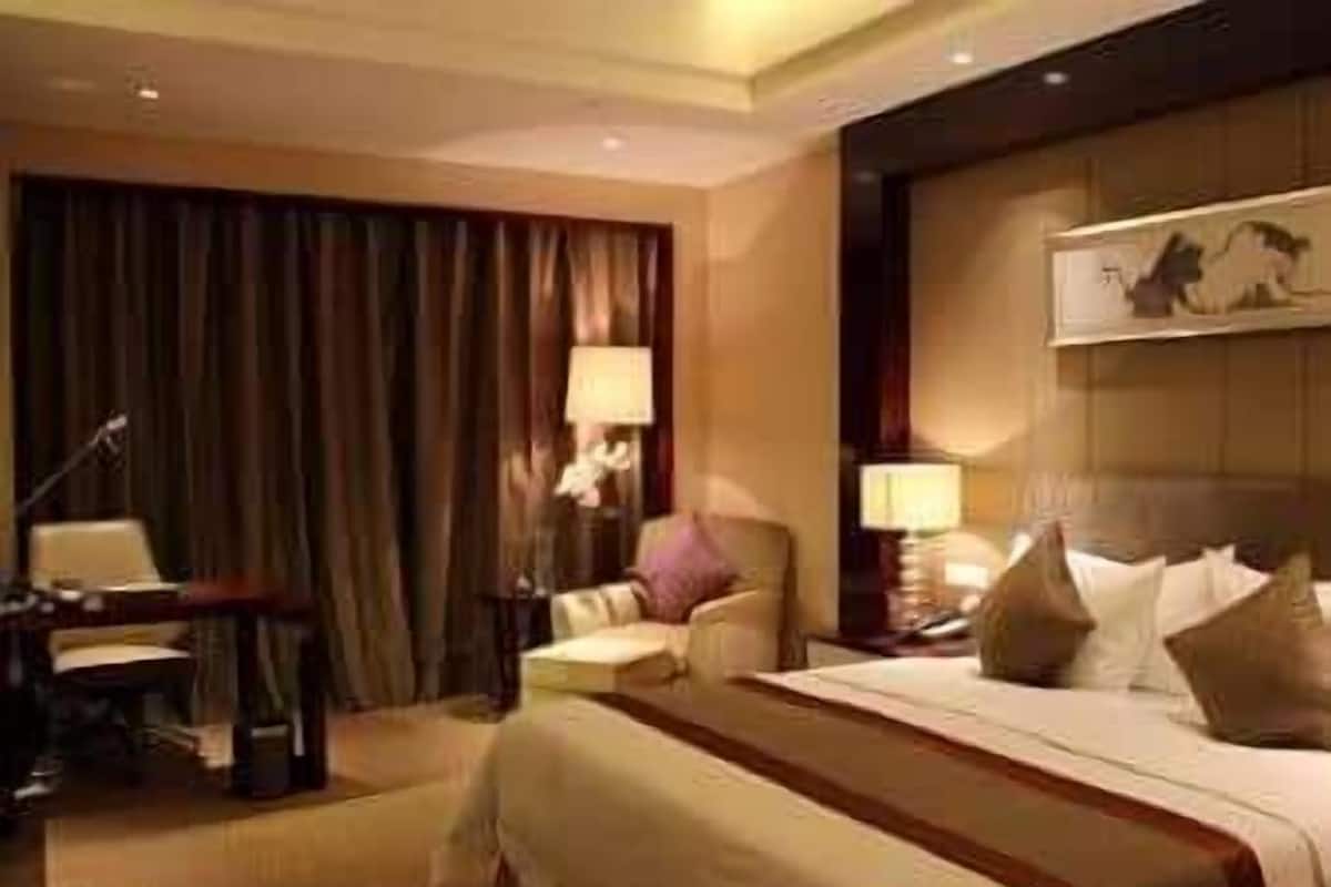 A hotel room with a large bed, a desk, a chair, and a lamp.