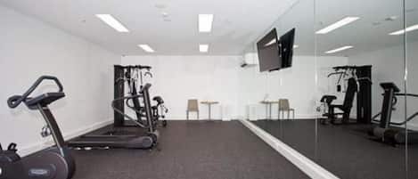 A gym with exercise equipment, a treadmill, and a mirrored wall.
