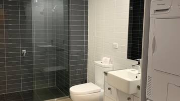 A modern bathroom with a glass-enclosed shower, a white toilet, a sink, and a washing machine.