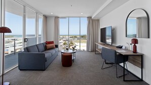 A modern hotel room with a large window, a sofa, a desk, a chair, a small table, and a TV. - Quest Mackay on Gordon (Mackay)