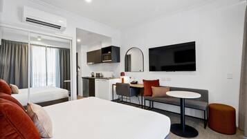Habitación de hotel con una cama grande, un sofá, una mesita, un televisor, un microondas y una kitchenette.
