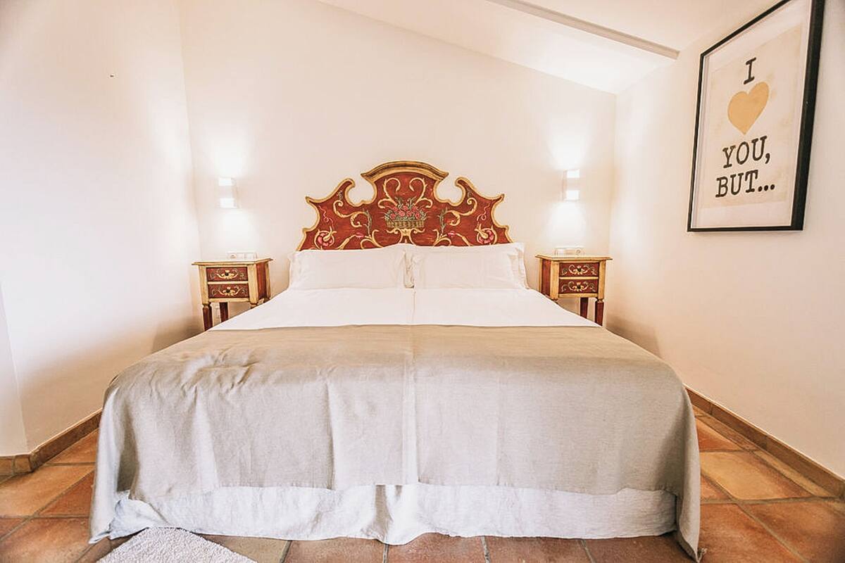 Una cama con cabecera decorativa, dos mesitas de noche y un cartel en la pared.