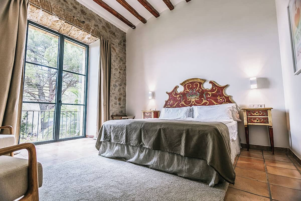 Quarto com uma cama grande, cabeceira de madeira, duas mesas de cabeceira e uma janela com vista para árvores.