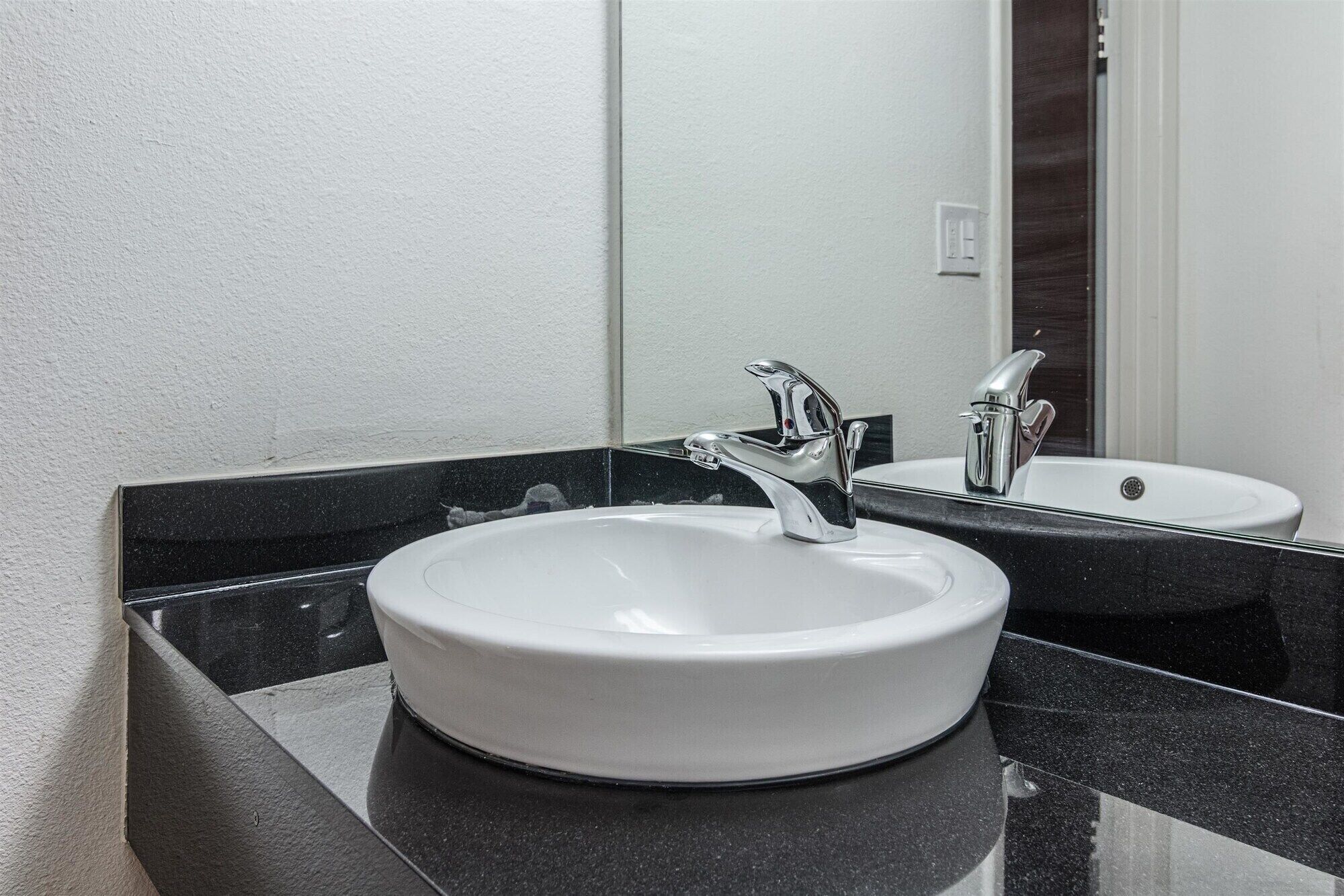 Un baño moderno con lavamanos blanco, encimera negra y un espejo grande.
