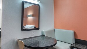 A small, modern bathroom with a round table, a cushioned bench, and a mirror with a light above it.